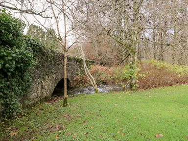 A stone bridge over a small river with trees and grass around at Scandale Bridge Cottage in Ambleside