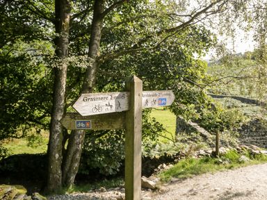 A wooden signpost with directions to Grasmere and Ambleside surrounded by trees and grass at Scandale Bridge Cottage in Ambleside