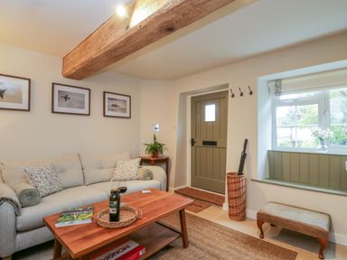A living room with a beige sofa coffee table and wooden door at Thorn Cottage in Fairford