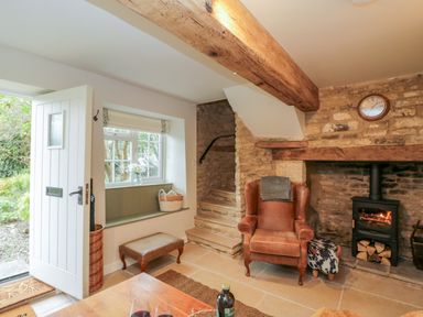An entrance area with a white door stone steps a leather armchair fireplace and window seat at Thorn Cottage in Fairford
