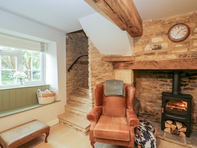 A sitting area with a leather armchair near a wood burning stove and stone stairs at Thorn Cottage in Fairford