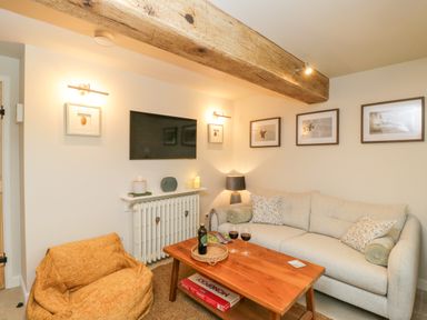 A living room with a beige sofa yellow bean bag wooden coffee table and wall mounted TV at Thorn Cottage in Fairford