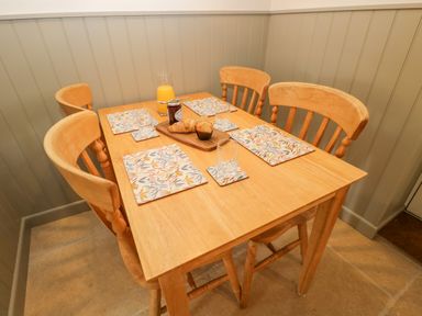 A wooden dining table with four chairs set with placemats glasses a jug of orange juice croissants and a jar of jam at Thorn Cottage in Fairford