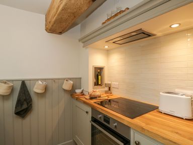 A kitchen countertop with an electric stovetop oven a toaster bread a bottle and hanging cloths at Thorn Cottage in Fairford