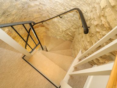 A spiral staircase with beige carpet and stone walls at Thorn Cottage in Fairford