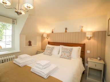 A bedroom with a double bed towels bedside tables and a window at Thorn Cottage in Fairford