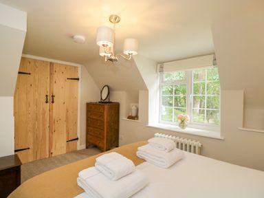 A bedroom with a bed folded towels wooden dresser window and wooden closet doors at Thorn Cottage in Fairford