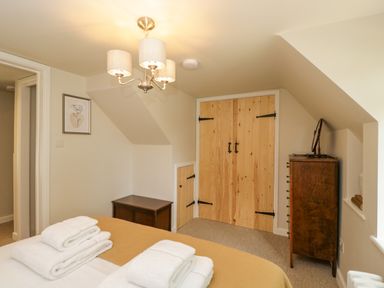 A bedroom with a bed towels wooden wardrobe and chest of drawers at Thorn Cottage in Fairford