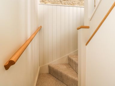 A carpeted staircase with wooden handrails and white panelled walls at Thorn Cottage in Fairford