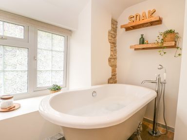 A bathroom with a freestanding bathtub near a window and wooden shelves on the wall at Thorn Cottage in Fairford