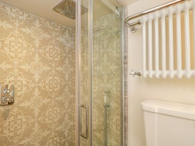 A shower area with patterned tiled walls and a glass door next to a white radiator and toilet at Thorn Cottage in Fairford
