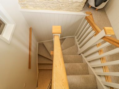 A carpeted staircase with wooden handrails and white balusters at Thorn Cottage in Fairford
