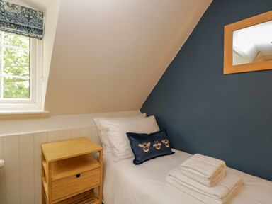 A bedroom with a single bed white bedding folded towels wooden bedside table and window at Thorn Cottage in Fairford