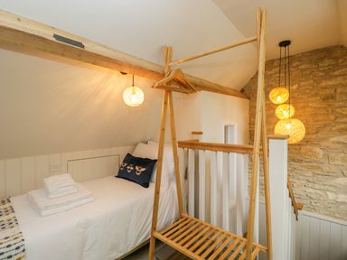 A small bedroom with a single bed folded towels a clothes rack and hanging lights at Thorn Cottage in Fairford