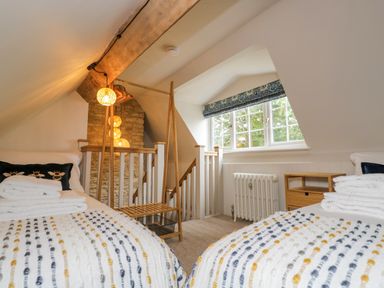 A bedroom with two single beds near a window and a wooden staircase at Thorn Cottage in Fairford