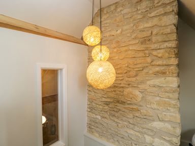 A stone wall with three hanging spherical lights and a mirror on an adjacent white wall at Thorn Cottage in Fairford