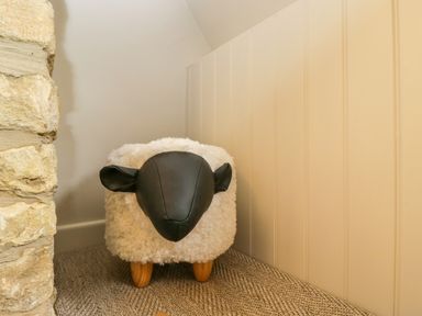 A corner with a sheep-shaped footstool next to a stone wall and paneled wall at Thorn Cottage in Fairford