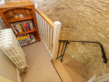 A stairway with stone walls a wooden bookshelf with books and games and a white radiator at Thorn Cottage in Fairford