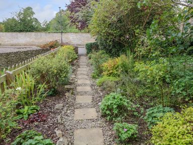 A garden path with stone tiles and plants on both sides at Thorn Cottage in Fairford