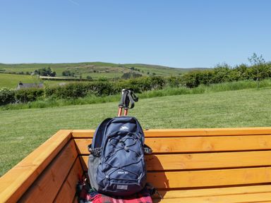 A blue backpack with walking poles on a wooden bench in a grassy field with hills and houses in the background at Holly in Ulverston