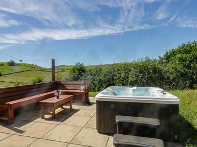 An outdoor area with a hot tub and wooden bench at Holly in Ulverston