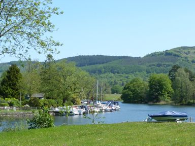 A river with boats docked near trees and hills in the background at Willow in Ulverston