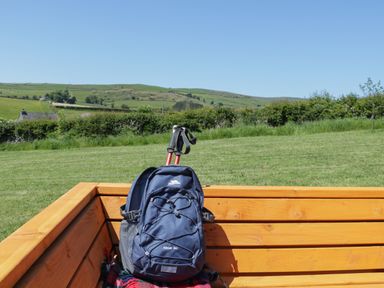 A wooden bench with a blue backpack and hiking poles in a grassy field with hills in the background at Oak in Ulverston
