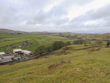 A rural landscape with farm buildings and pod-style cabins on green fields surrounded by hills at Rowan in Ulverston
