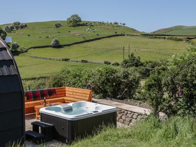 An outdoor hot tub next to wooden seating and green fields with grazing cows at Rowan in Ulverston