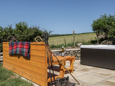 An outdoor patio with a wooden bench, walking sticks, boots, a bottle of wine and glasses next to a hot tub at Rowan in Ulverston