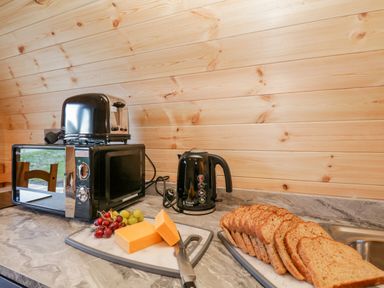 A kitchen counter with a black microwave, black toaster, black kettle, cheese, grapes, and sliced bread at Cherry in Ulverston
