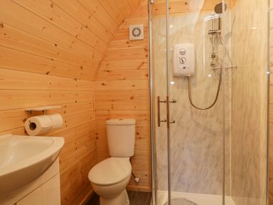 A bathroom with a toilet sink and enclosed shower in a wooden paneled room at Cherry in Ulverston