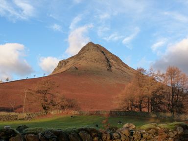 A mountain with rocky slopes and sparse trees with a stone wall and grassy field with sheep at Cherry in Ulverston