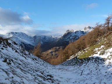 A snow-covered mountain valley with sparse trees and rocky slopes under a blue sky at Cherry in Ulverston