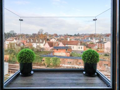View of rooftops and houses from a balcony with glass railing and two potted plants at Woodbridge Penthouse in Woodbridge