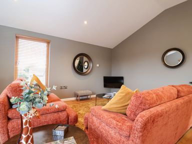A living room with two orange sofas and a wall-mounted TV at Woodbridge Penthouse in Woodbridge