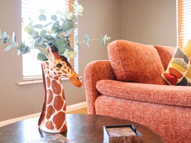 A ceramic giraffe vase with green leaves on a table next to an orange sofa with a patterned pillow in a living room at Woodbridge Penthouse in Woodbridge