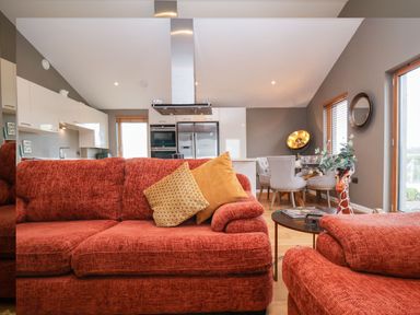 A living room with red sofas and yellow cushions near a kitchen with white cabinets and a dining area at Woodbridge Penthouse in Woodbridge