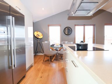 A kitchen with a stainless steel refrigerator a dining table with chairs a stove with a pot and large windows at Woodbridge Penthouse in Woodbridge