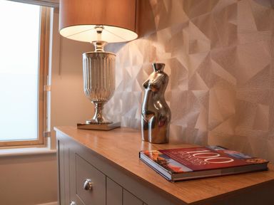 A wooden cabinet with a table lamp a small statue and a book titled 100 wonders of the world on top at Woodbridge Penthouse in Woodbridge