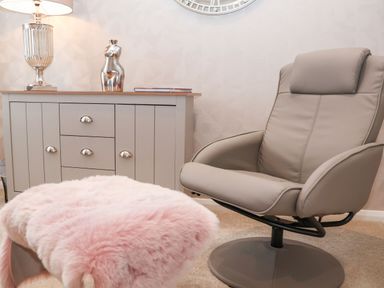 A room with a gray swivel chair pink fur-covered stool and a gray cabinet with a lamp and decorative sculpture on top at Woodbridge Penthouse in Woodbridge