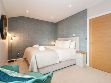 A bedroom with a large bed with white bedding bedside table with drawers a round mirror and a green armchair at Woodbridge Penthouse in Woodbridge
