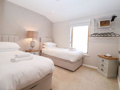 A bedroom with two single beds bedside tables a lamp a window and a wall-mounted rack with hangers at Woodbridge Penthouse in Woodbridge