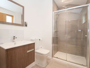 A bathroom with a wooden vanity unit with sink a toilet and a glass enclosed shower at Woodbridge Penthouse in Woodbridge