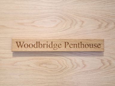 A wooden plaque with the text Woodbridge Penthouse on a wooden surface Woodbridge Penthouse Woodbridge