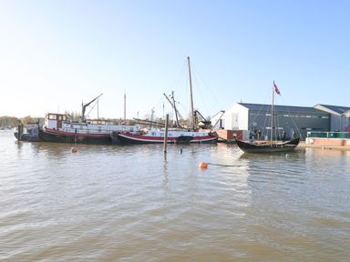 A harbor with several moored boats and a building with people near the water at Woodbridge Penthouse in Woodbridge