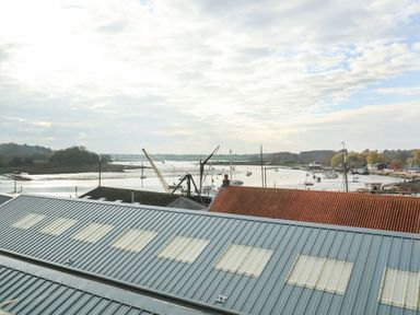 A view of a harbor with boats and cranes behind metal and tiled rooftops at Woodbridge Penthouse in Woodbridge