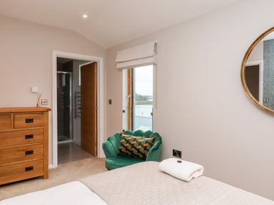A bedroom with a wooden dresser green armchair with a patterned pillow a bed with a blanket and towel and a round mirror on the wall at Woodbridge Penthouse in Woodbridge