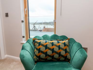 A green armchair with a patterned cushion in front of a window with a view of a marina at Woodbridge Penthouse in Woodbridge