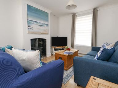 A living room with two blue sofas a wooden chest coffee table a television and a painting of the sea at Day Cottage in Weymouth